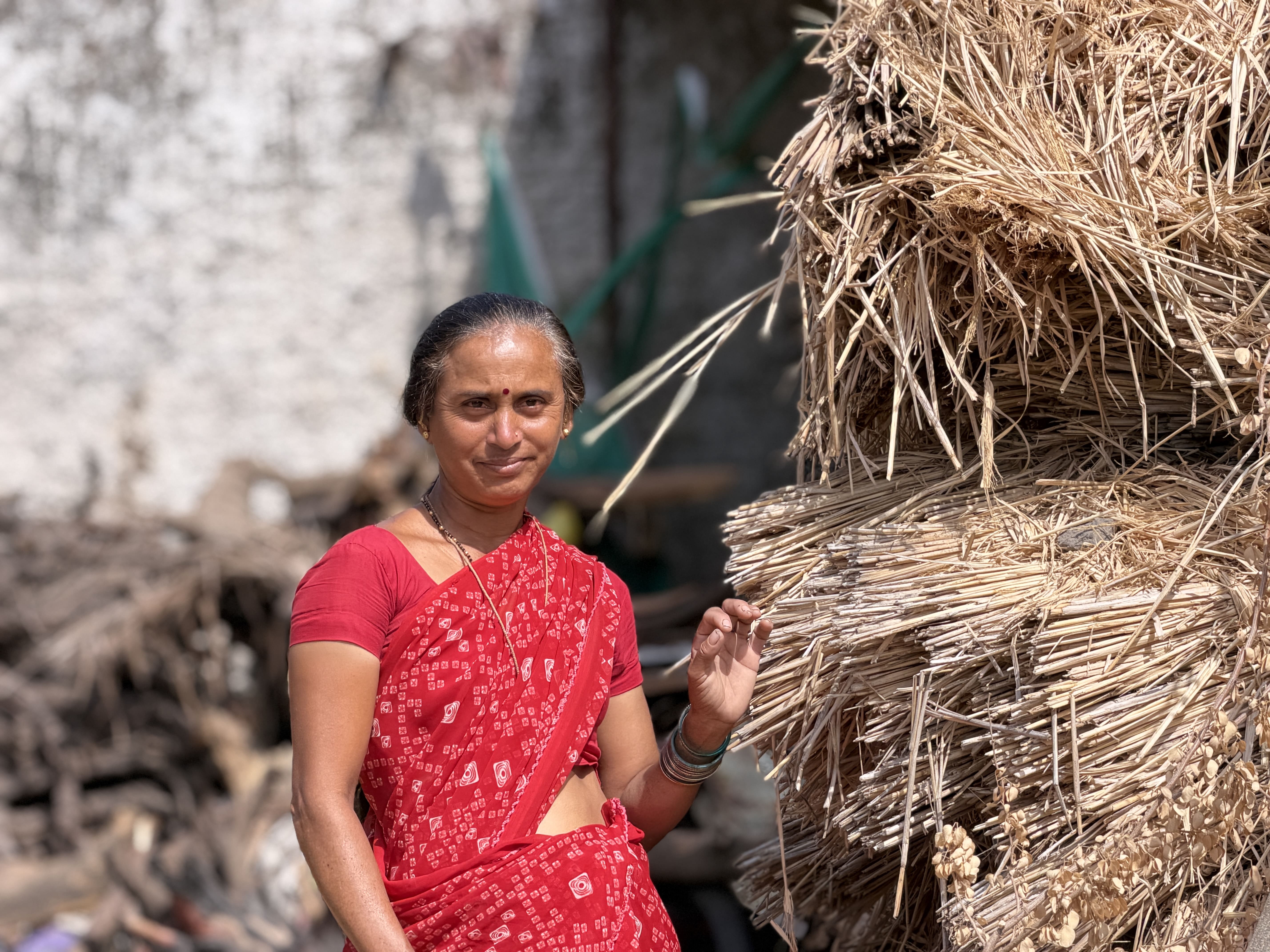 Rural woman in red sari standing beside stacked agricultural residue